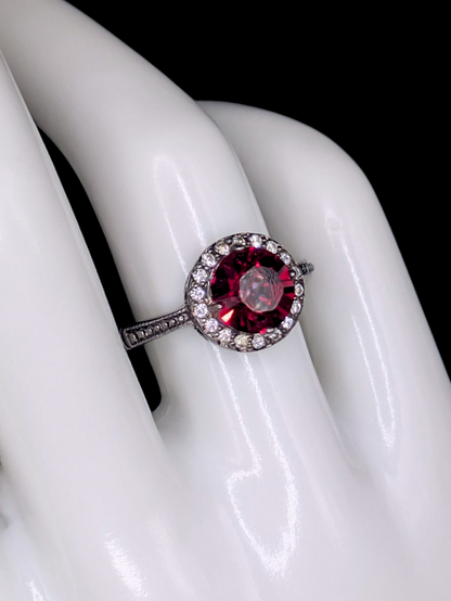 Vintage Inspired Round Single Cut Simulated Ruby Solitaire with Simulated Diamond Halo on Intricate Mount Oxidized Silver Toned Ring